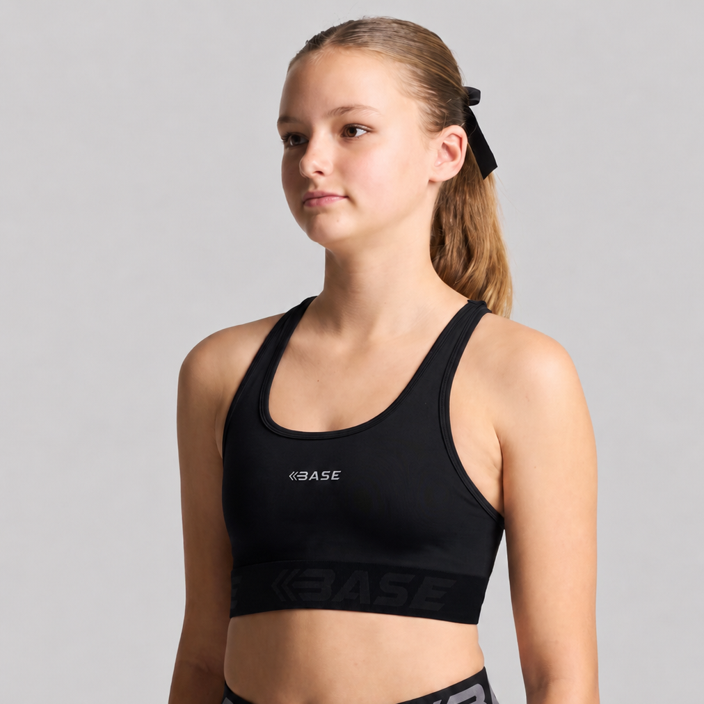 A young female model wearing a black BASE sports bra and matching black athletic shorts with gray logo accents, posed against a solid gray studio background.