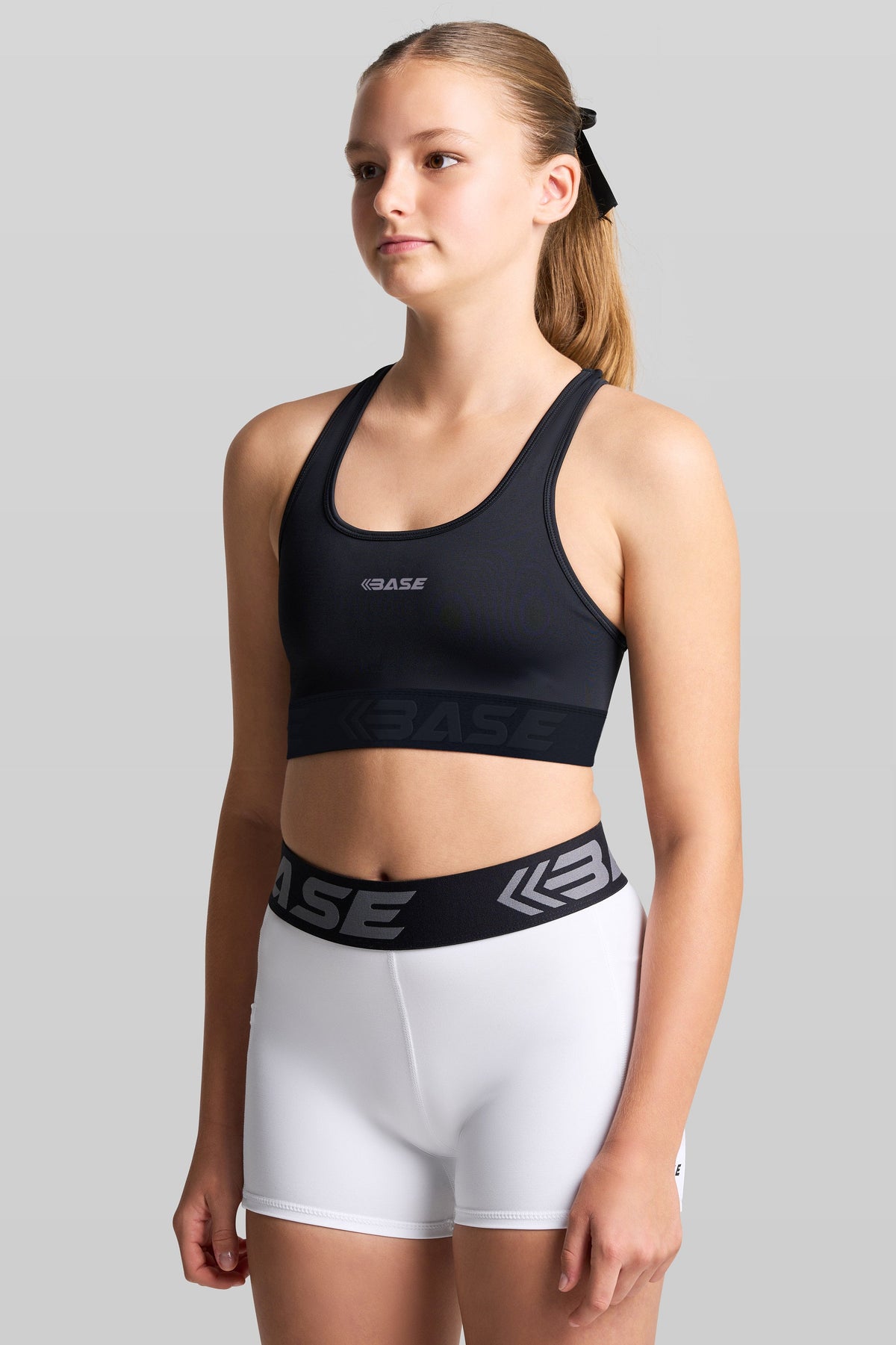 Person wearing a black sports bra and white shorts with 'BASE' branding on a gray background