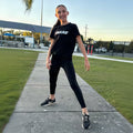 Person wearing a black t-shirt with 'BASE' logo and black leggings on a sidewalk.