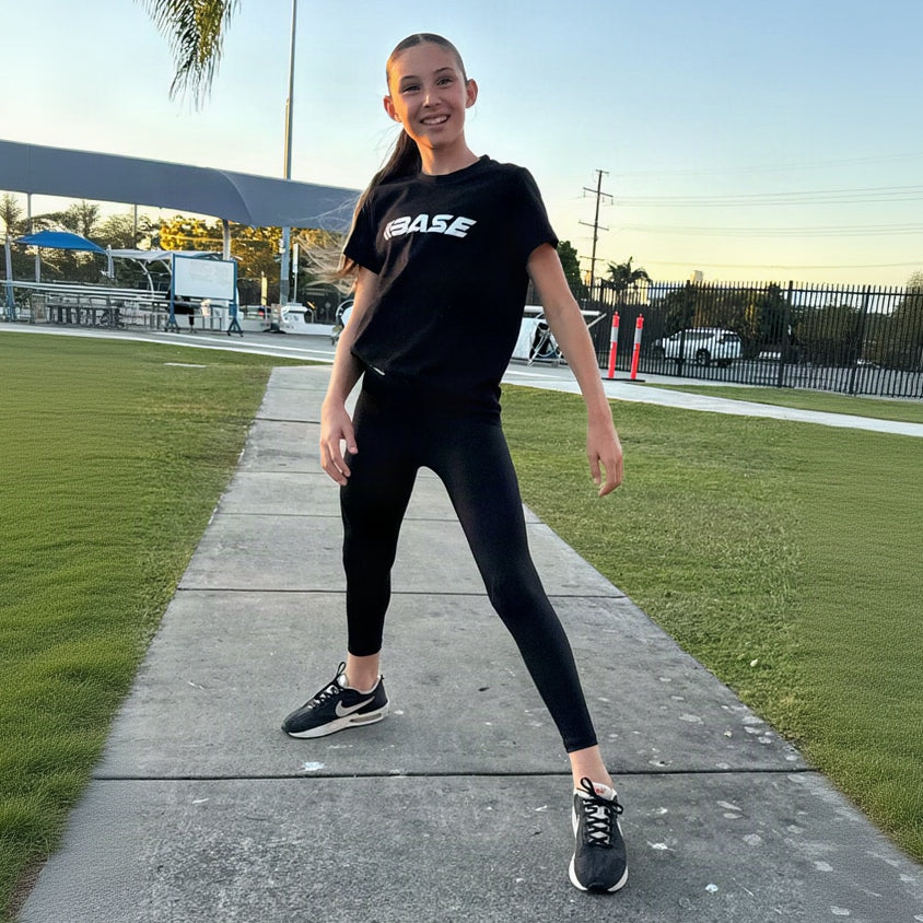 Person wearing a black t-shirt with 'BASE' logo and black leggings on a sidewalk.